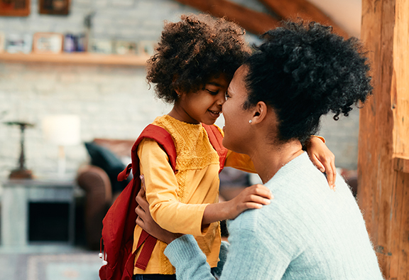 Affectionate African mother talking to her small daughter while saying goodbye before going to school for the first time.