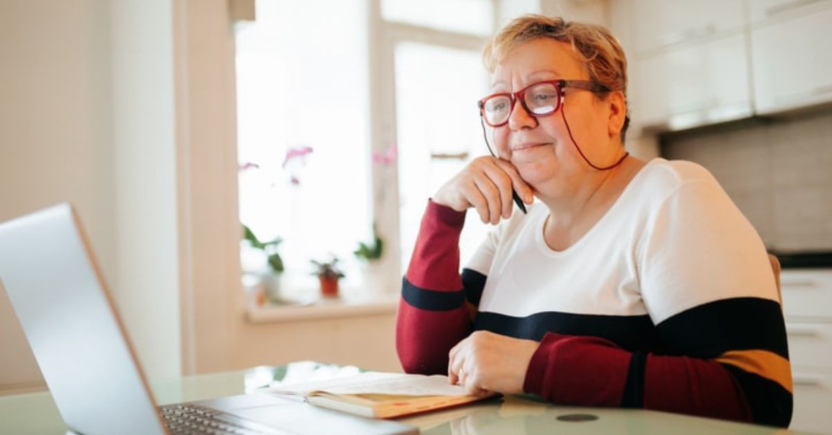 An elderly woman with short hair and glasses sits at her laptop reading about how to find a trustworthy diabetes supply company.