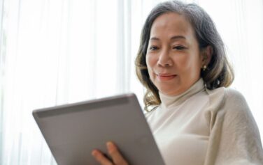 A 65 year old Asian woman looks at medicare deductible FAQs on her tablet.