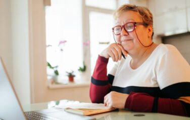 An elderly woman with short hair and glasses sits at her laptop reading about how to find a trustworthy diabetes supply company.